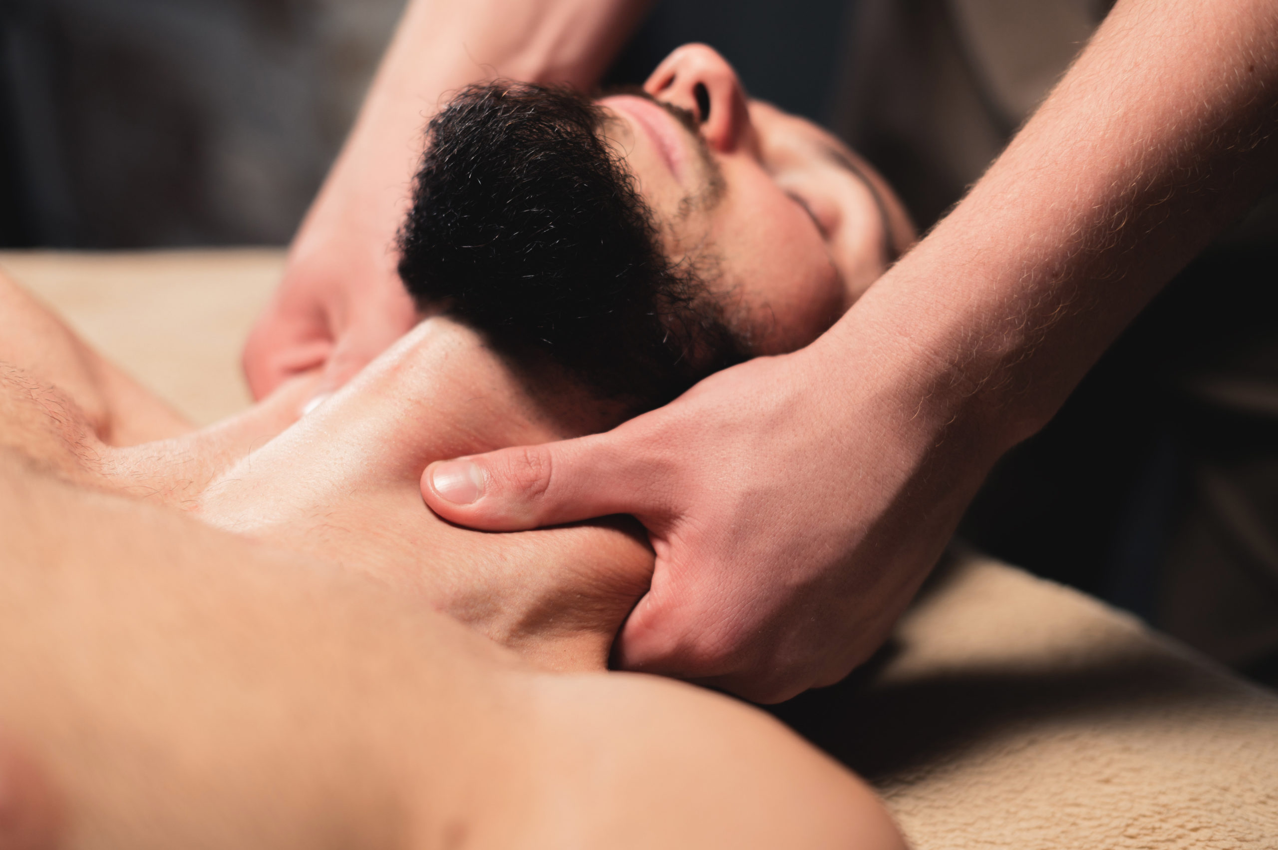 Close-up Professional neck massage to a bearded male athlete in a dark room of a spa massage room.