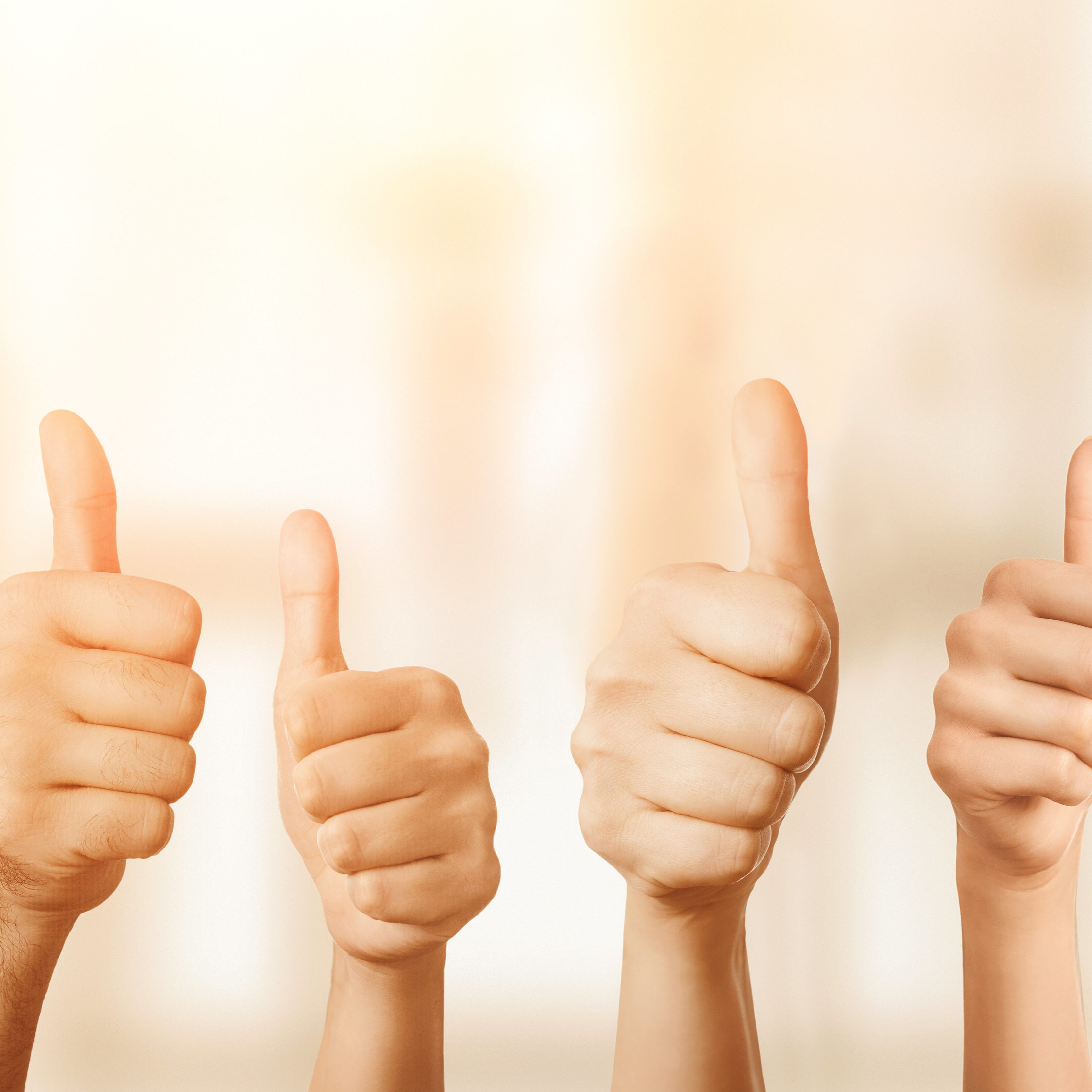 Close up of group of hands showing thumbs up over defocused background with copy space